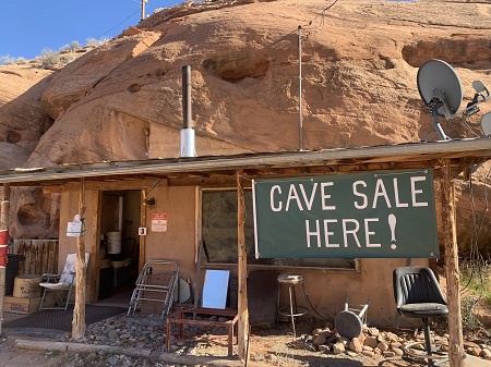 shows a rustic home carved out of the rock, located along the Colorado River near Moab, UT. Sign says cave sale here.